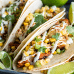 A plate of chili lime chicken tacos garnished with fresh cilantro, avocado slices, and lime wedges, served with a side of colorful salsa.