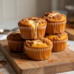 Close-up of freshly baked pumpkin cream cheese muffins with crumb topping on a rustic wooden table.