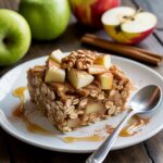 A warm, golden-brown apple cinnamon baked oatmeal in a glass baking dish, topped with chopped walnuts and fresh apple slices.