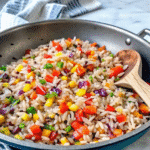 Colorful bowl of Rainbow Fried Rice with vibrant vegetables and eggs, garnished with green onions.