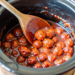 A slow cooker full of Crock Pot Grape Jelly Meatballs coated in glossy grape jelly and chili sauce.