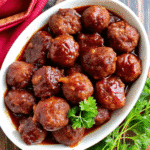Close-up of tender Slow Cooker Cranberry Chili Meatballs coated in a glossy sweet and spicy cranberry chili sauce in a slow cooker.