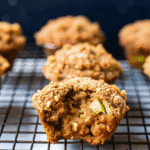 Freshly baked One Bowl Apple Cinnamon Muffins with golden tops and visible apple chunks, served on a wire rack.