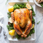 Golden Roast Thanksgiving Turkey on a carving board with fresh herbs and lemon.