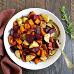 Golden roasted root vegetables including yams, red potatoes, carrots, beets, and parsnips with rosemary and thyme
