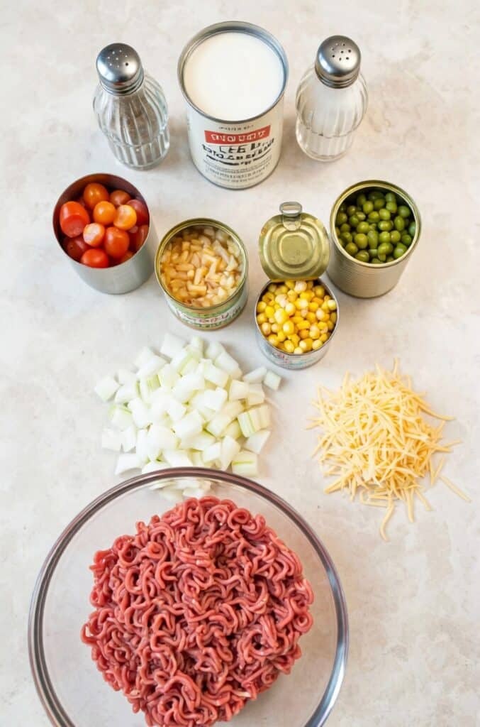 Ingredients for Slow Cooker Cowboy Casserole including ground beef, chopped onion, diced tomatoes, corn, green beans, cream of mushroom soup, and shredded cheddar cheese.