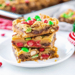 Freshly baked Christmas Magic Cookie Bars with chocolate chips, coconut, pecans, and red and green M&Ms on a parchment-lined pan