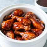 Crock pot chicken drumsticks coated in a sticky barbecue sauce, garnished with chopped parsley, served hot in a slow cooker.