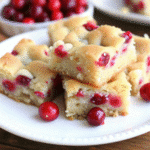 Cranberry Christmas Cake sliced into small squares, showcasing a golden crumb filled with bright red cranberries.