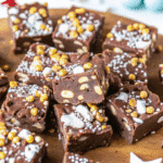 Christmas Tiffin squares on a festive plate, topped with white chocolate drizzle and colorful holiday sprinkles.