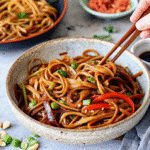 A colorful Vegetable Noodle Stir Fry with egg noodles, bell peppers, broccoli, and zucchini, garnished with sesame seeds and green onions.