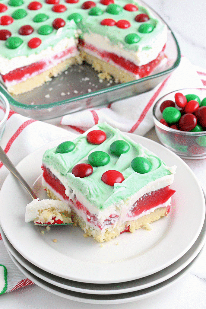 Sliced Christmas Lush showing colorful layers of pistachio pudding, cream cheese, and Oreo crust on a serving plate.