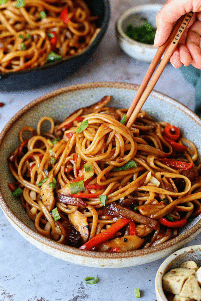 Close-up of a freshly cooked Vegetable Noodle Stir Fry in a wok, showing glossy noodles and assorted vegetables.