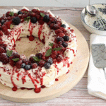 Christmas Pavlova Wreath topped with whipped cream, fresh berries, pomegranate seeds, and mint on a holiday serving platter.