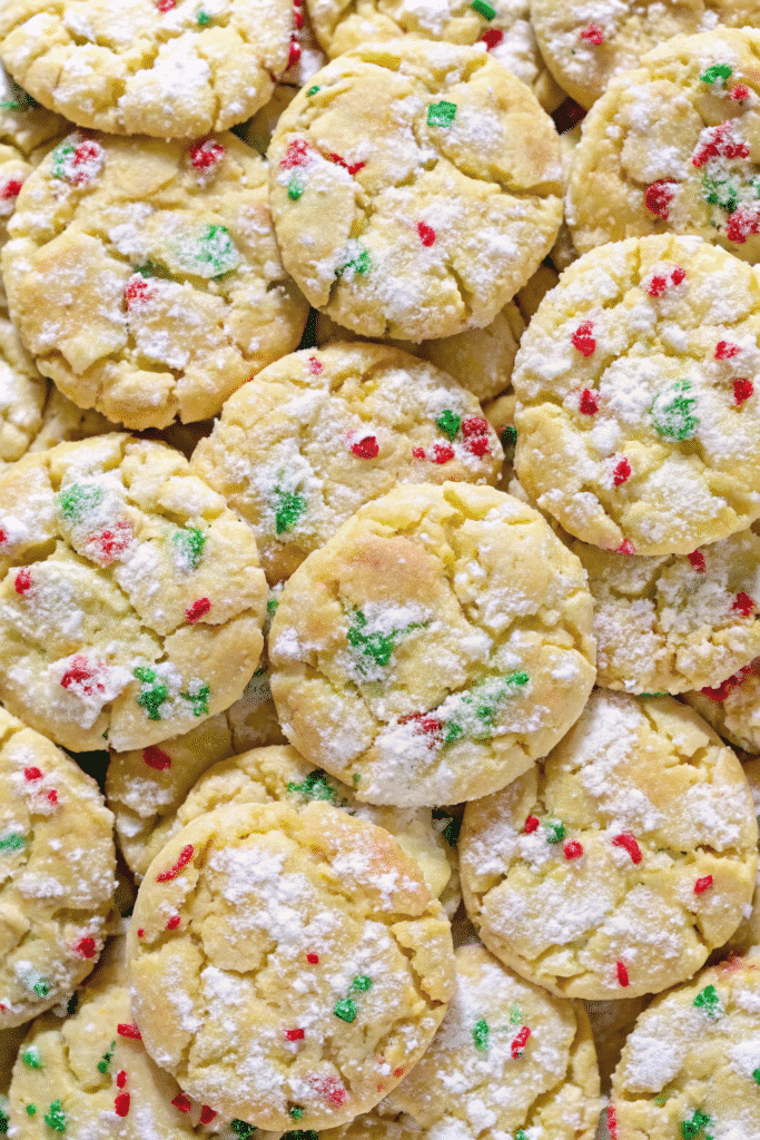 A plate of Christmas Ooey Gooey Butter Cookies, golden edges with gooey centers and festive holiday sprinkles.