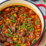 Hearty beef and vegetable stew in a Dutch oven filled with tender beef chunks, potatoes, carrots, peas, and green beans in a rich broth.