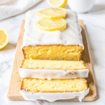 Slice of moist lemon cake with lemon icing on top, sitting on a cooling rack.