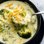 Creamy Crockpot Broccoli Cheese Soup served in a bowl with melted cheddar and fresh broccoli florets on top.
