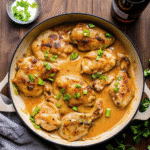Skillet Bang Bang Chicken Thighs coated in creamy Bang Bang sauce and garnished with chopped green onions in a pan