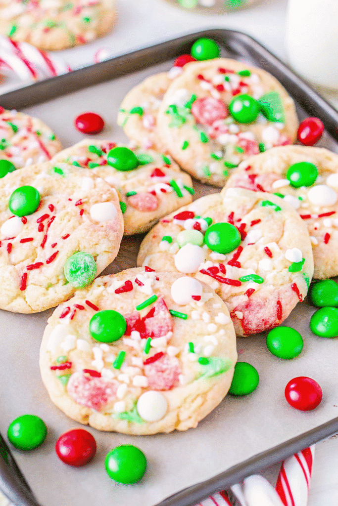 Close-up of colorful Christmas Cake Mix Cookies cooling on parchment paper with melted white chocolate chips and candy pieces.