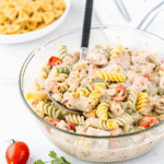 A bowl of creamy Chicken Bacon Ranch Pasta Salad with spiral pasta, crispy bacon, shredded cheddar, chopped chicken, zucchini, and cherry tomatoes.