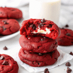A stack of freshly baked Red Velvet Cream Cheese Cookies showing a creamy, soft filling inside, sprinkled with mini chocolate chips.