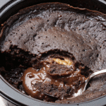 Warm Crockpot Chocolate Lava Cake with melted chocolate and chocolate chips on top, served with a scoop of vanilla ice cream.