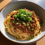 A bowl of Ground Turkey Hot Honey Noodle Bowl topped with sliced green onions and sesame seeds, showcasing glossy, sweet-spicy turkey over noodles.