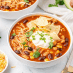 A steaming bowl of 7 Can Chicken Taco Soup with beans, corn, diced chicken, and colorful garnishes of cilantro, cheese, and tortilla chips.