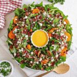 Colorful Christmas Salad with spring mix, mandarin oranges, pomegranate seeds, candied pecans, and crumbled feta on a festive platter.