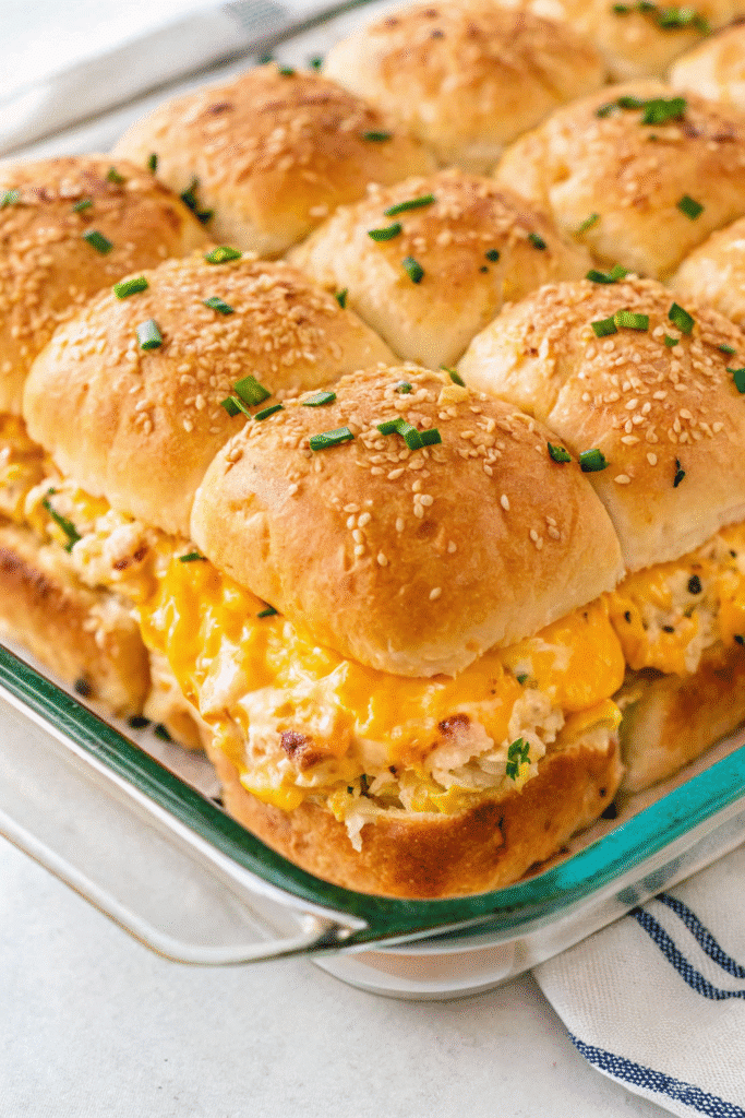 Close-up of freshly baked Crack Chicken Sliders with gooey cheese, crispy bacon, and buttery tops on a tray.
