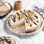 Slice of creamy No Bake Peanut Butter Pie topped with whipped cream and chopped peanuts in a graham cracker crust