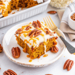 Moist Pumpkin Poke Cake topped with cream cheese frosting, caramel drizzle, and chopped pecans in a 9x13 pan.