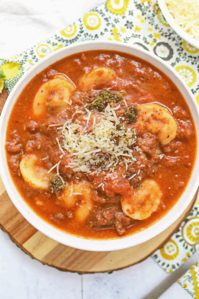 Close-up of Instant Pot Pesto Tomato Tortellini Soup served in a white bowl, showing vibrant tomato broth and green pesto.