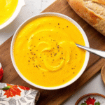 Creamy Acorn Squash Soup served in a bowl, garnished with a swirl of sour cream and roasted squash pieces.