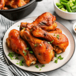 Slow Cooker Chicken Drumsticks coated in sticky barbecue sauce, served on a plate with a side of extra sauce.