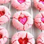 Pink Valentine Crinkle Cookies dusted with powdered sugar and topped with heart sprinkles on a baking tray.