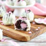 Valentine Cookie Balls with Oreos coated in smooth vanilla almond bark and decorated with festive sprinkles on parchment paper.