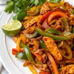 Air fryer basket filled with seasoned chicken strips, red, yellow, and green bell peppers, and onions cooked to perfection.