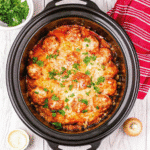 Slow cooker filled with meatball casserole topped with melted mozzarella and Parmesan cheese.
