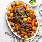 Crock Pot Pot Roast with carrots, potatoes, and gravy served in a slow cooker.