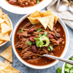 Bowl of Crock Pot Chili Con Carne with Shredded Beef topped with shredded cheese and chopped onions.
