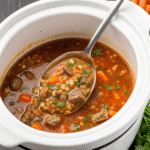 A bowl of Crock Pot Beef Barley Soup with tender beef, carrots, celery, and barley in a rich broth, garnished with fresh parsley.