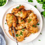 Golden brown boneless air fryer chicken thighs served on a plate with herbs.