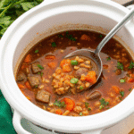 A bowl of Crock Pot Beef Barley Soup with tender beef chunks, carrots, celery, and pearl barley in a rich broth, garnished with fresh parsley.