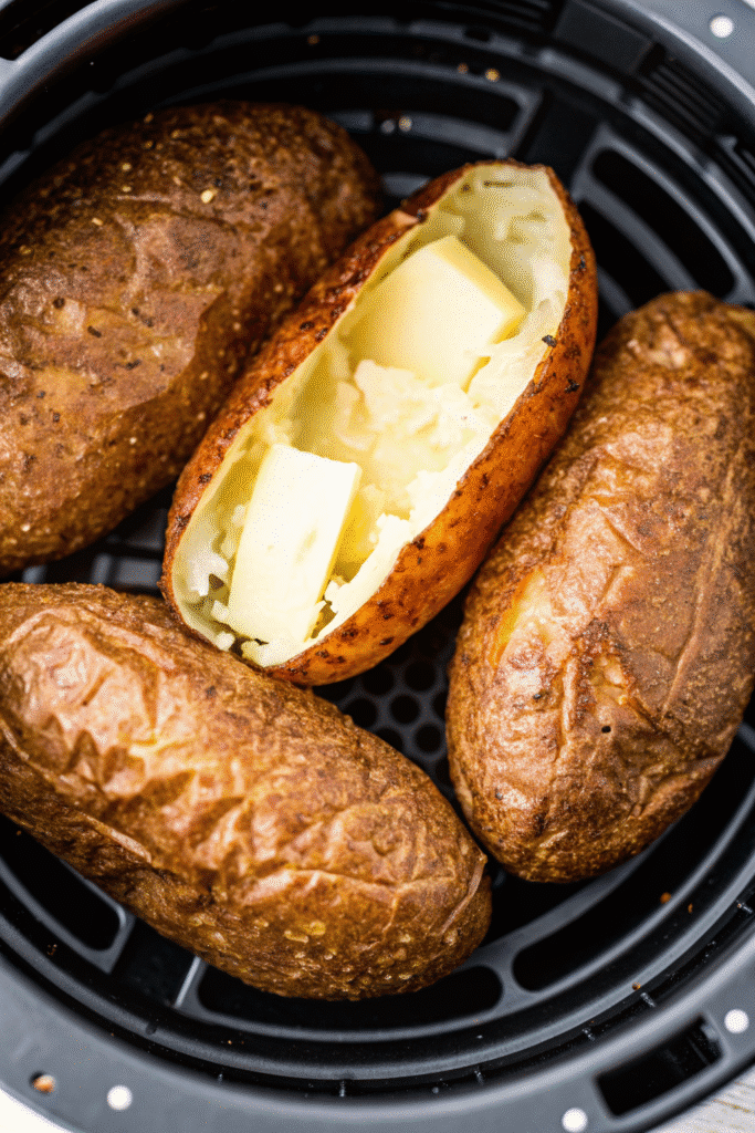 Three russet potatoes cooked in an air fryer, with golden-brown skin and steaming fluffy centers, ready to serve.