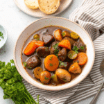 Slow cooker filled with Honey Balsamic Beef Stew, featuring tender beef, baby potatoes, and colorful carrots in a rich glossy sauce.