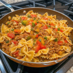 A skillet filled with colorful stuffed pepper pasta, featuring bowtie pasta, diced bell peppers, ground beef, and rich tomato sauce.