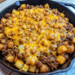 Crispy tater tots layered over savory sloppy joe mixture with melted cheddar cheese in a skillet