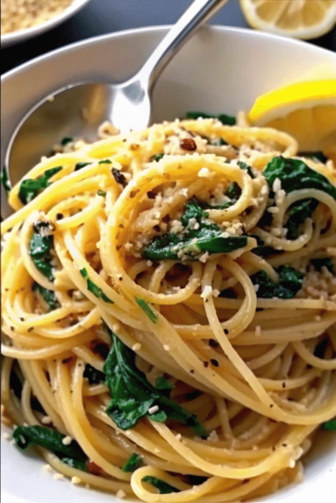 Freshly cooked spaghetti mixed with wilted spinach, golden garlic slices, and Parmesan cheese served in a rustic bowl.